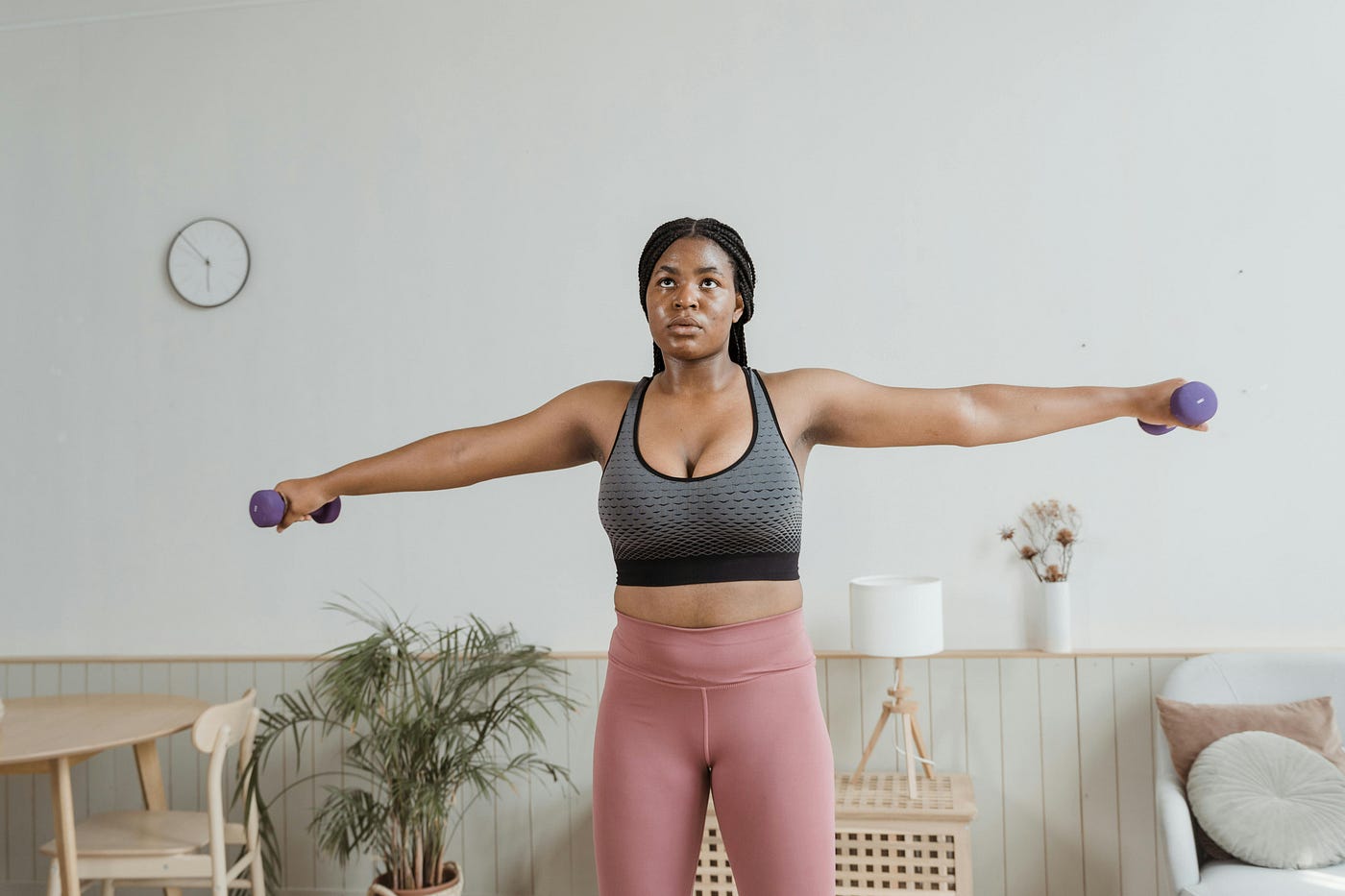 Woman doing lateral raises with light dumbbells at home, arms extended out to her sides at shoulder height