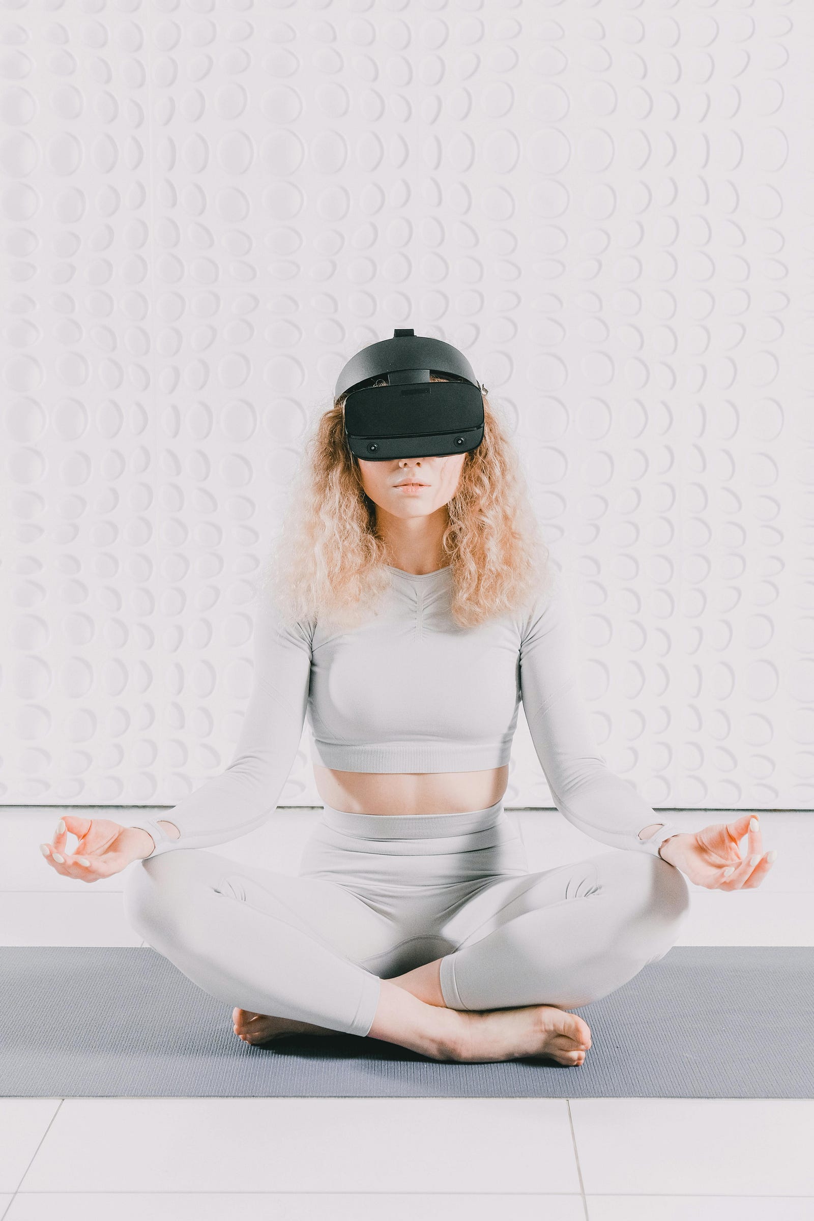 Woman wearing a VR headset, sitting cross-legged on a yoga mat in a meditation pose
