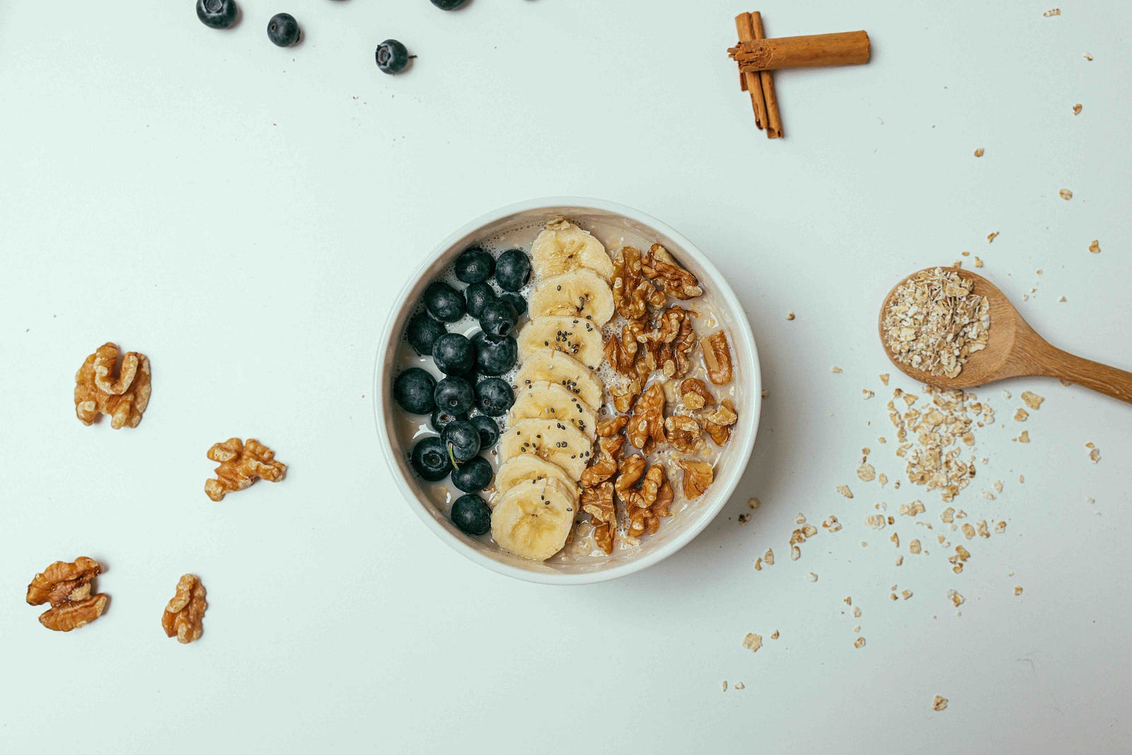 Bowl of oatmeal topped with blueberries, sliced banana, chia seeds and walnuts, with rolled oats on a wooden spoon